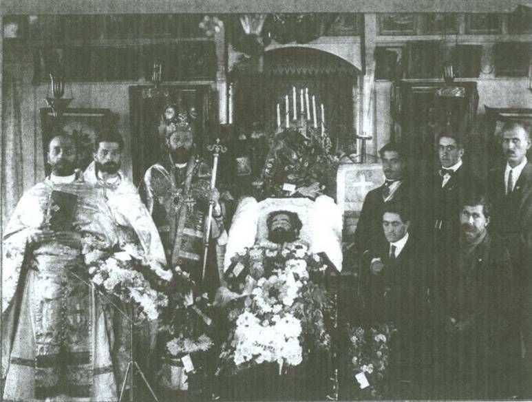 Father Nicola lying in state before the iconostasis, with a bishop, clergy and parishioners standing beside him