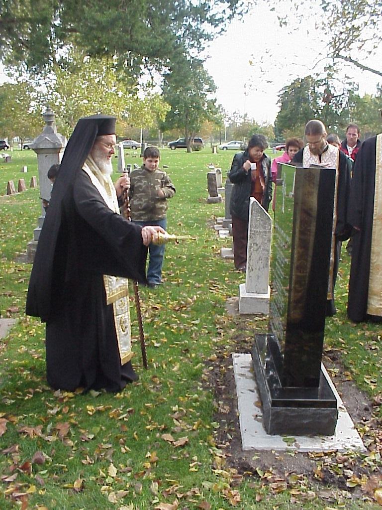 A bishop censing Father Nicola’s black granite headstone in the cemetery, with clergy and faithful gathered round