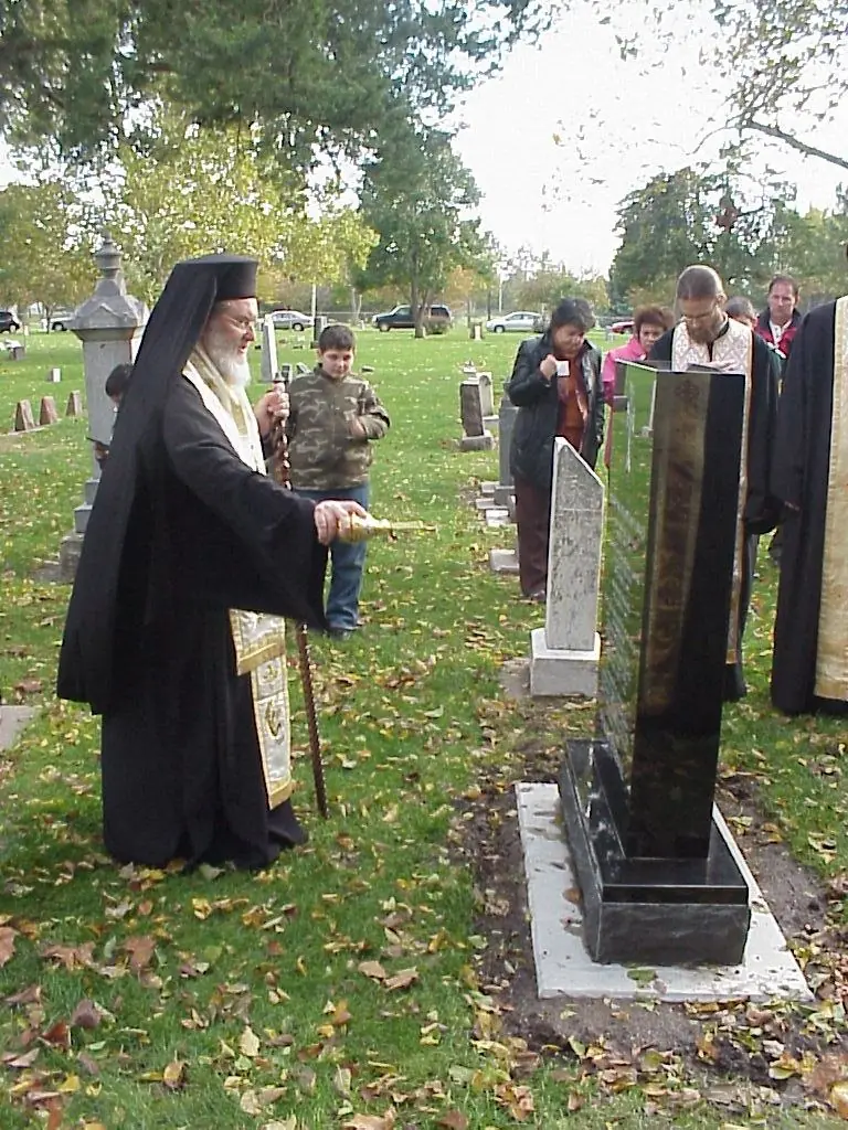 A bishop censing Father Nicola&rsquo;s black granite headstone in the cemetery, with clergy and faithful gathered round